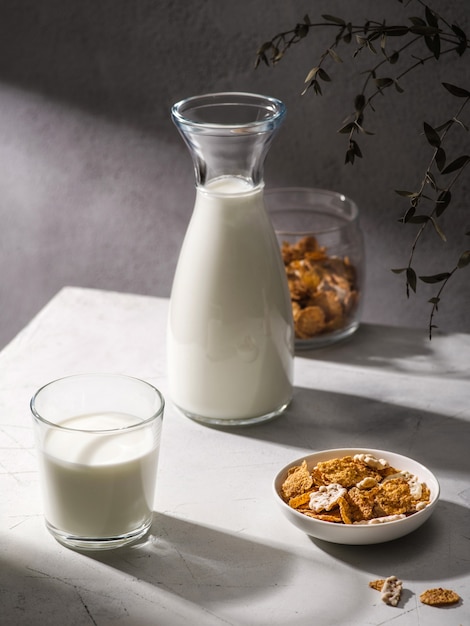 Sana colazione con cornflakes e latte. Bicchiere di latte e ciotola con gustosi cornflakes su sfondo grigio. Luce dura, ombra.