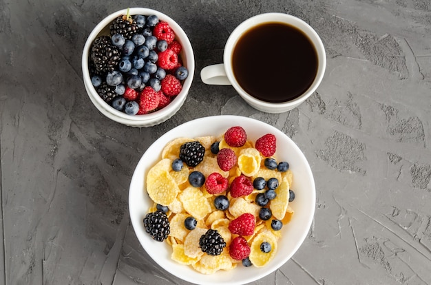 Sana colazione con cornflakes in un piatto bianco, bacche e caffè