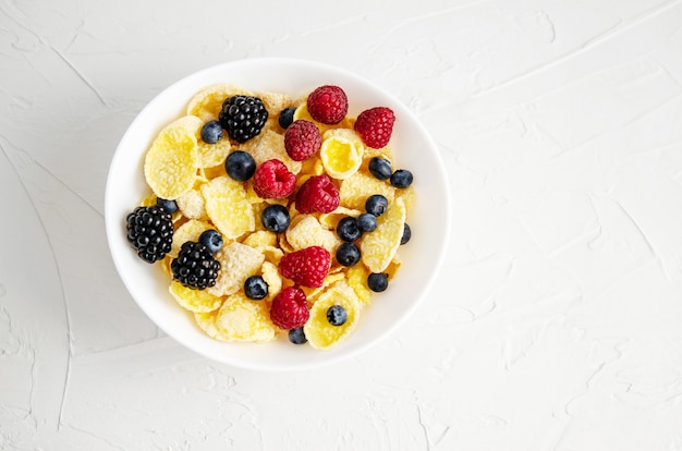 Sana colazione con cornflakes in un piatto bianco, bacche, latte e caffè