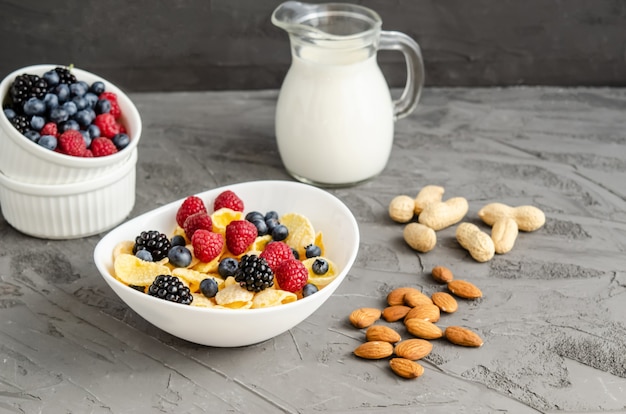 Sana colazione con cornflakes in un piatto bianco, bacche, latte e noci