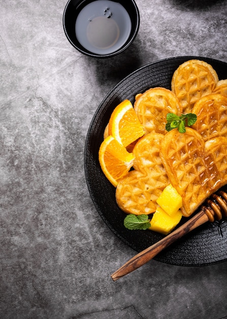 Sana colazione con cuori di cialde calde fresche, fiori di frittelle con miele di bacche e frutti esotici su superficie grigia, vista dall'alto, piatto laici. Concetto di cibo