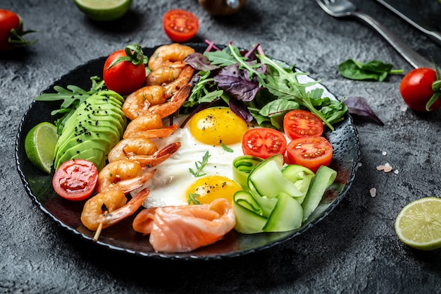 Sana colazione con salmone, gamberi alla griglia, gamberi, uova fritte, insalata fresca, pomodori, cetrioli e avocado. dieta chetogenica. Vista dall'alto.