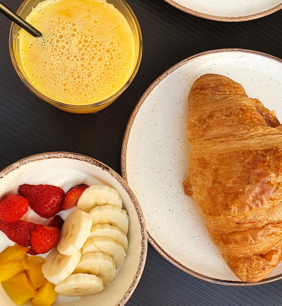 Sana colazione con yogurt naturale con croissant di frutta e succo d'arancia su tavola nera