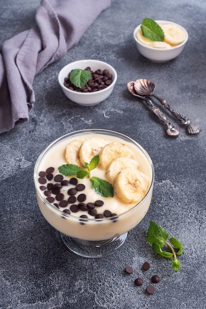 Sana colazione, dessert con banana yogurt al latte e cioccolato su un piatto. Sfondo di cemento scuro.