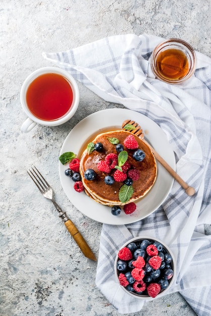 Sana colazione estiva, frittelle americane classiche fatte in casa con bacche fresche e miele, vista superiore superficie di pietra grigio chiaro mattina