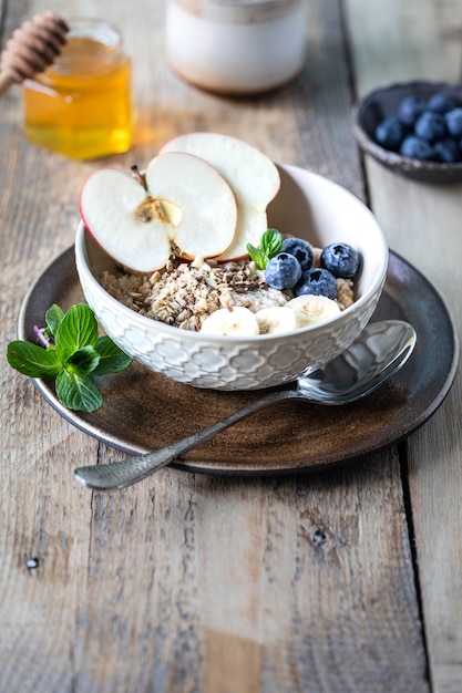 Sana colazione, farina d'avena o muesli con mirtilli, mela e miele su un fondo di legno rustico. Copia spazio