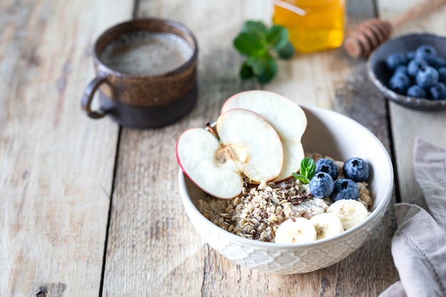 Sana colazione, farina d'avena o muesli con mirtilli, mela e miele su un fondo di legno rustico. Copia spazio