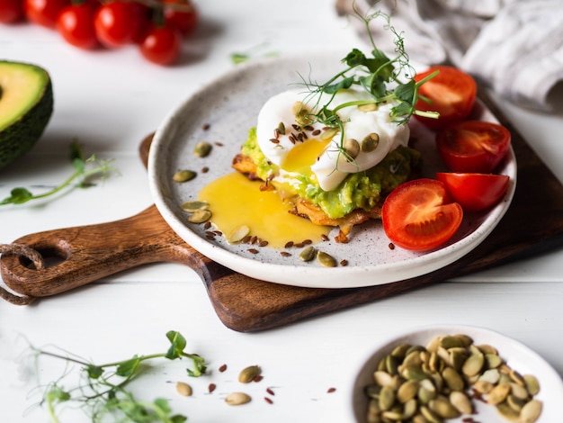 Sana colazione nutriente di pancake di patate, avocado schiacciato, uovo in camicia, germogli di pisello e vari semi su un piatto di ceramica