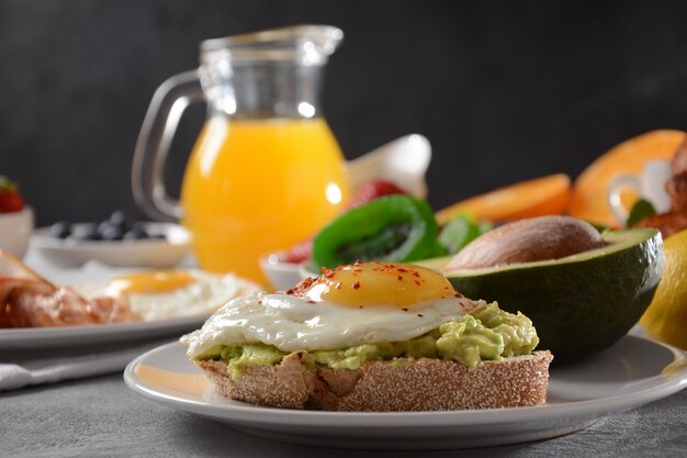 Sana colazione Toast con avocado e uova, bacon e uova, frutta fresca e secca, succo fresco