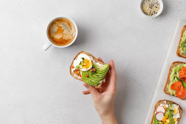 Sana colazione toast con avocado Una mano con avocado toast Tazza di caffè sul tavolo