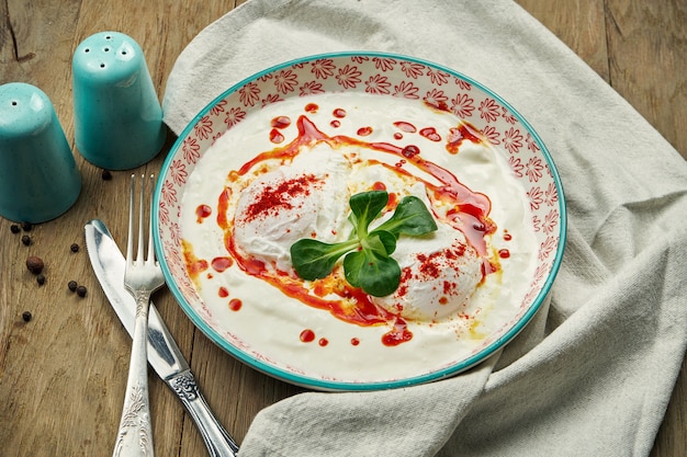 Sana colazione - uovo in camicia con salsa di yogurt in una ciotola blu su un tavolo di legno. Cilbir