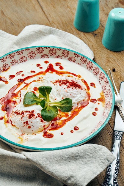 Sana colazione - uovo in camicia con salsa di yogurt in una ciotola blu su una superficie di legno. Cilbir