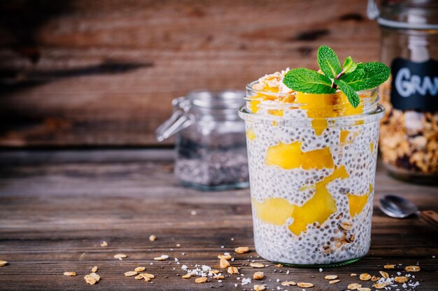 Sana colazione vegana budino di chia con mango e muesli nel barattolo su fondo rustico in legno