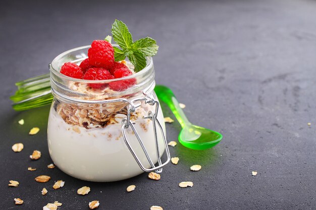 Sana colazione: yogurt con muesli e lamponi su uno sfondo nero
