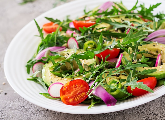 Sana insalata di verdure fresche - pomodori, avocado, rucola, ravanello e semi su una ciotola. Cibo vegano.