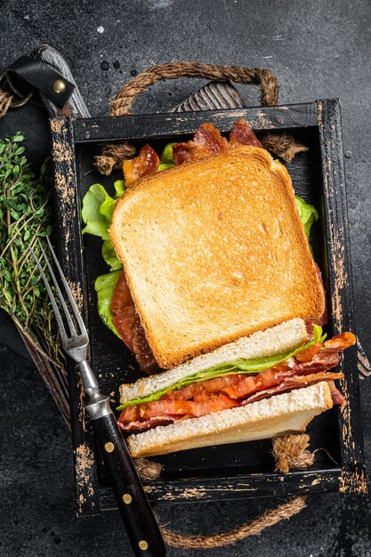 Sandwich BLT tostato fatto in casa con pancetta, pomodoro e lattuga in vassoio di legno Sfondo nero Vista dall'alto