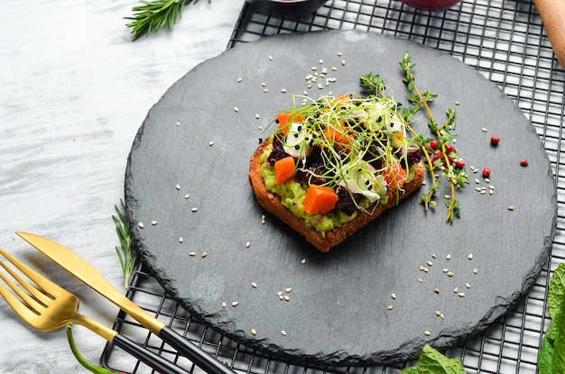 Sandwich ciabatta avocado barbabietole e carote Colazione su una lastra di pietra nera