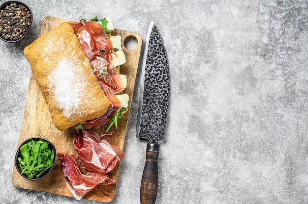 Sandwich di ciabatta con prosciutto crudo, rucola e formaggio brie camembert. Tavolo grigio. Vista dall'alto. Copia spazio.