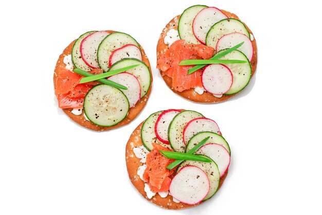 Sandwich di cracker con salmone, cetriolo, radice, formaggio cottage e cipolle verdi isolate