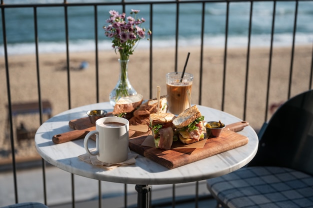 Sandwich di pollo e caffè ghiacciato con cioccolata calda e fiori in vaso su un tavolo di marmo nella caffetteria vicino alla spiaggia al mattino