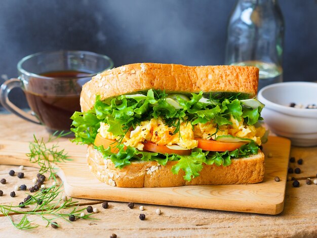 Sandwich di uova strapazzate con pomodoro fresco, cetriolo e lattuga verde per una sana colazione.
