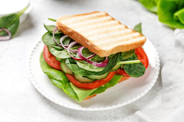 Sandwich di verdure con lattuga verde biologica pomodori e spinaci su piatto bianco Primo piano