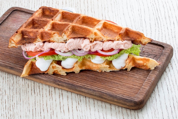 Sandwich di waffle con crema di salmone pomodori e insalata su fondo di legno chiaro