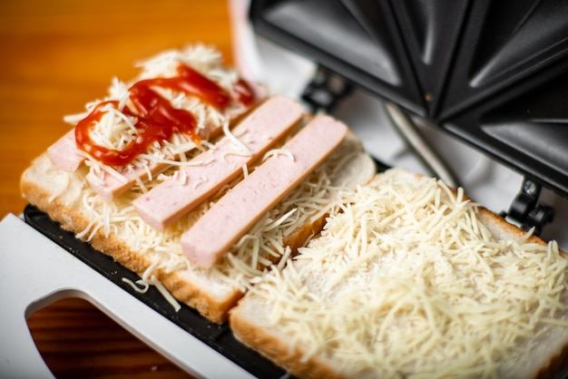 Sandwich maker aperto con toast al formaggio e salsicce Sandwiching