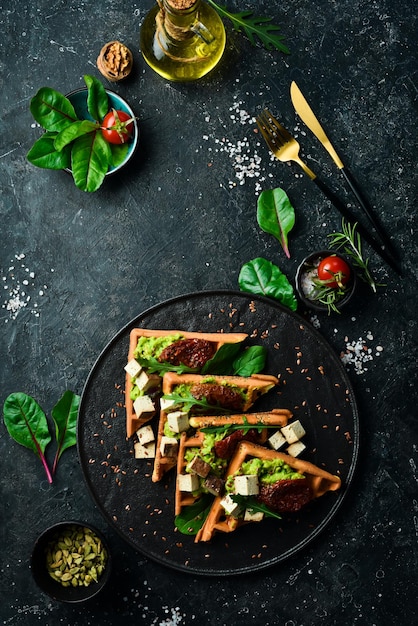 Sandwich per colazione cialde belghe con patè di avocado pomodori secchi e formaggio tofu Il concetto di nutrizione dietetica su uno sfondo di pietra