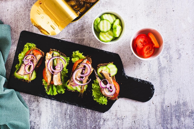 Sandwich su pane di segale con pomodori, cetrioli, sprat e cipolle su ardesia