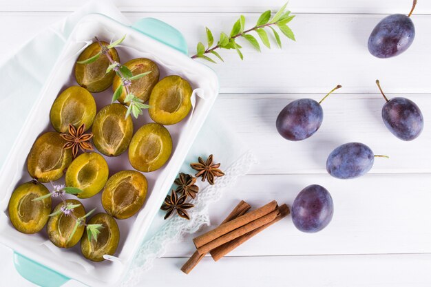 Sano dessert fatto in casa. Prugne rosse affettate pronte per la cottura in una teglia con menta fresca, cannella, anice