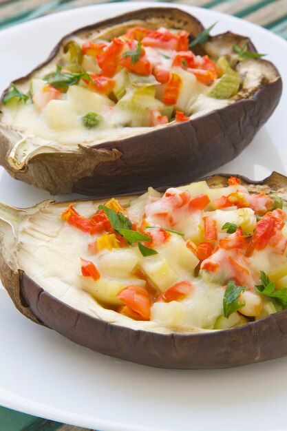 Sano pranzo vegetariano: melanzane ripiene al forno con verdure e formaggio su un piatto bianco.