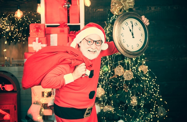 Santa Claus allegro che tiene l'orologio sveglia sul camino e sullo sfondo dell'albero di Natale