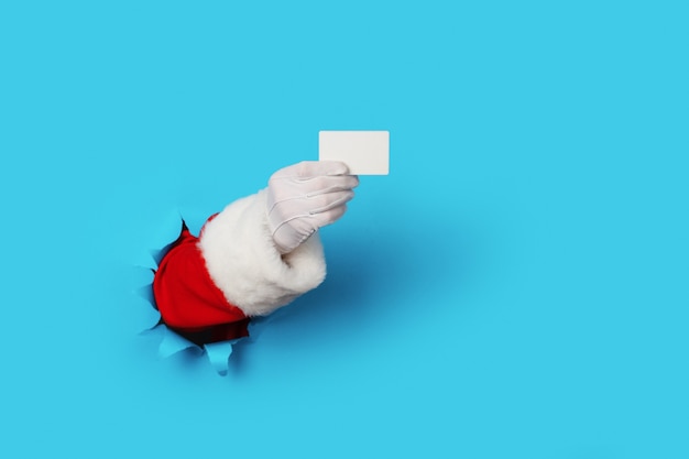 Santa Claus che tiene una carta bianca in bianco isolata sopra azzurro. Acquisti, vendite, regali per i concetti del Black Friday, Natale e Capodanno 2020.