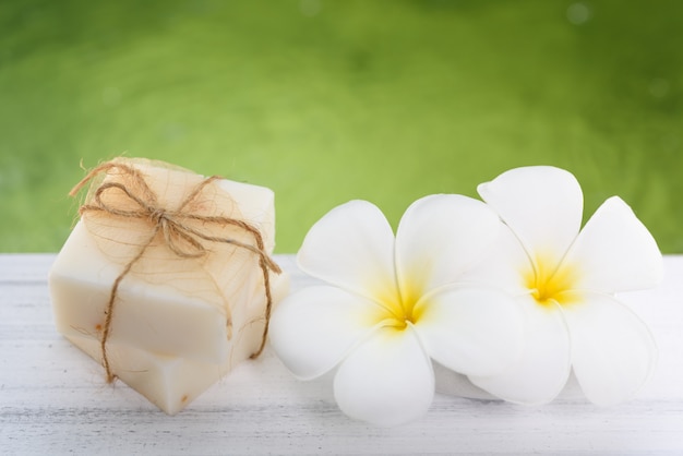 Sapone al latte della stazione termale e fiori del frangipane sulla tavola di legno bianca