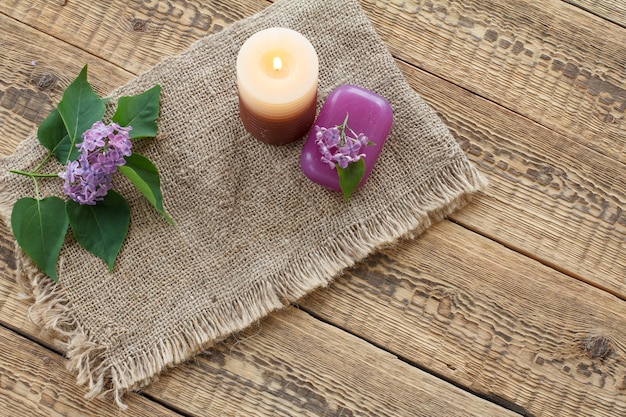 Sapone per procedure da bagno candele accese e fiori lilla su tela di sacco e vecchie tavole di legno