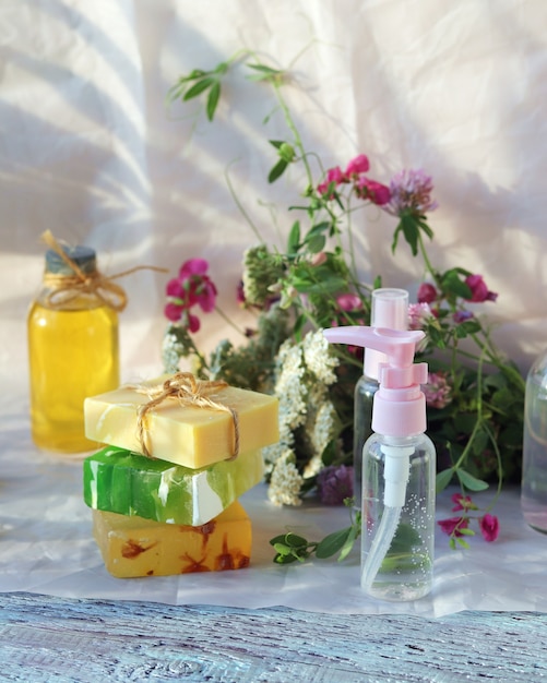 Sapone, spray, bouquet di erbe medicinali e bottiglie di vetro con olio aromatico su un tavolo di legno