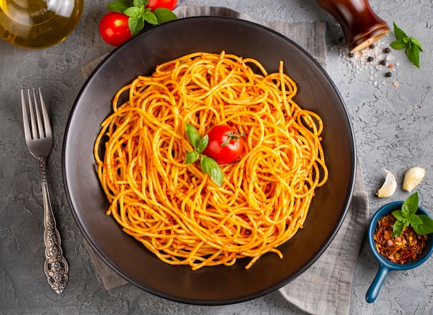 Saporita e appetitosa pasta di spaghetti italiana classica con salsa di pomodoro formaggio parmesano e basilico sul piatto e ingredienti per la cottura della pasta su un tavolo di marmo bianco