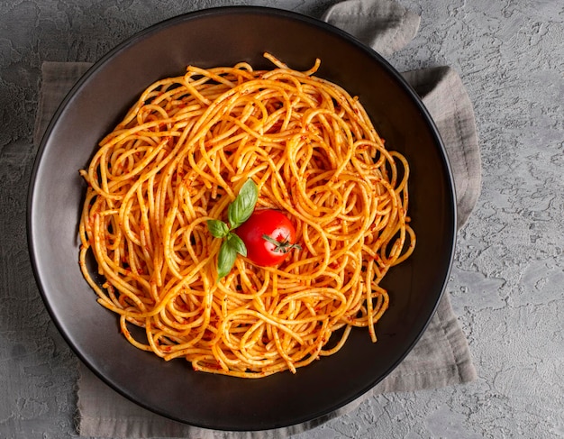 Saporita e appetitosa pasta di spaghetti italiana classica con salsa di pomodoro formaggio parmesano e basilico sul piatto e ingredienti per la cottura della pasta su un tavolo di marmo bianco