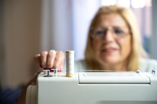 Sarta donna con gli occhiali seduta mentre prepara il filo della sua macchina da cucire