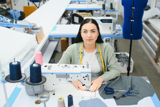 Sarta femminile felice che lavora con la macchina da cucire alla fabbrica tessile