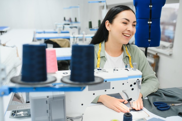 Sarta femminile felice che lavora con la macchina da cucire alla fabbrica tessile