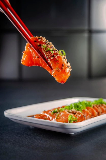 Sashimi di salmone sulle bacchette con salsa di sesamo, shoyu e miso su un tavolo nero. Avvicinamento.