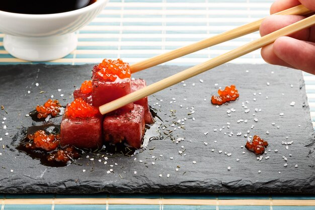 Sashimi di tonno immerso in salsa di soia con uova di salmone, sale denso e aneto su pietra di ardesia con bacchette