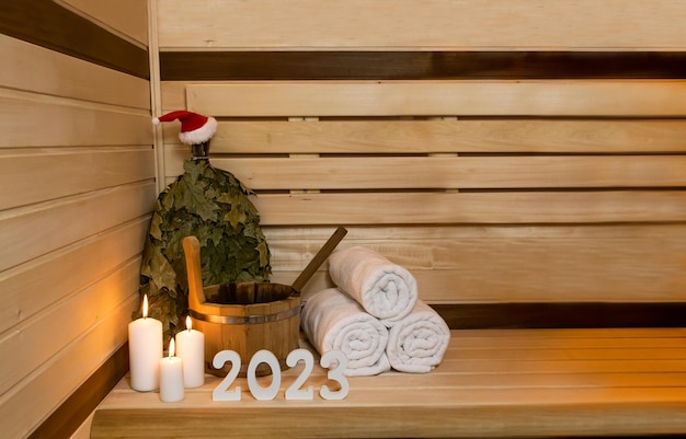 Sauna. 2023 figure sono in piedi, un secchio di legno, candele, una scopa cappello di Babbo Natale.copia spazio, testo.