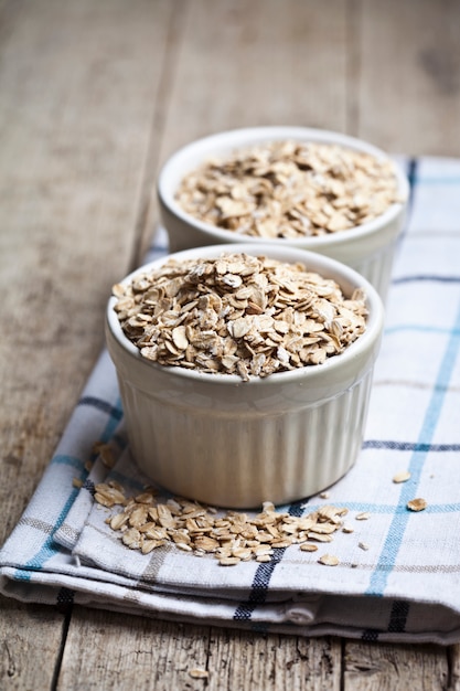 Scaglie di avena cruda in ciotole di ceramica sul tovagliolo di lino, spighe di grano dorato