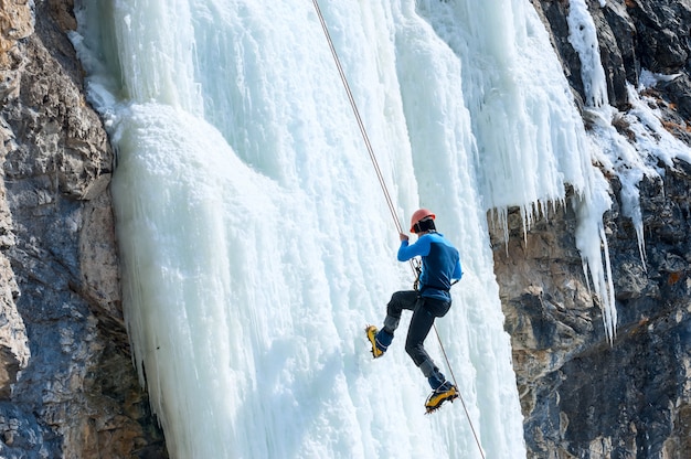 Scalatore che scende la corda con una cascata ghiacciata