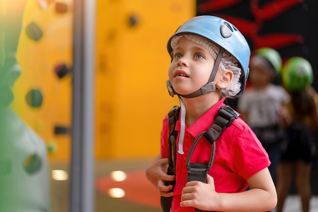 Scalatore della bambina sveglia in casco protettivo blu e attrezzatura per l'arrampicata