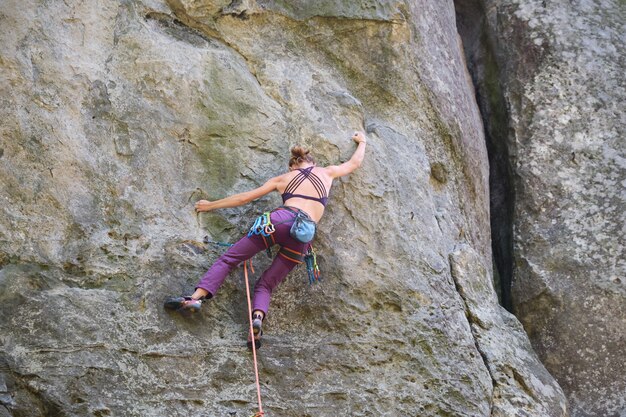 Scalatore determinato della ragazza che si arrampica sulla parete ripida della montagna rocciosa. Sportiva superando percorso difficile. Impegnarsi in sport estremi e concetto di hobby di arrampicata su roccia.