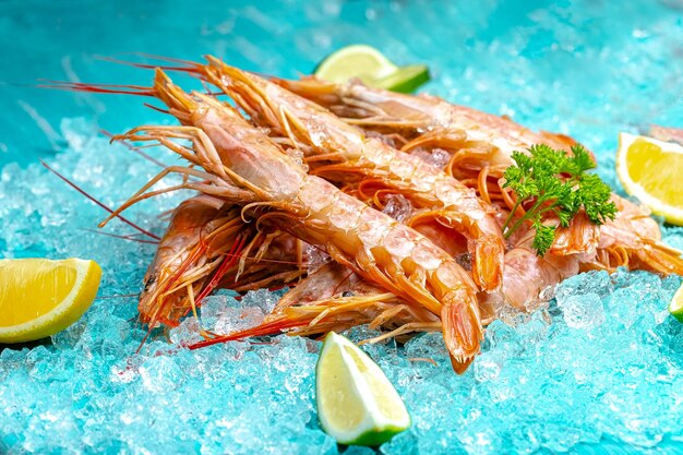 scampi di gamberi freschi rossi con e senza testa, giacciono sullo sfondo del mare blu ghiaccio, ciliegia